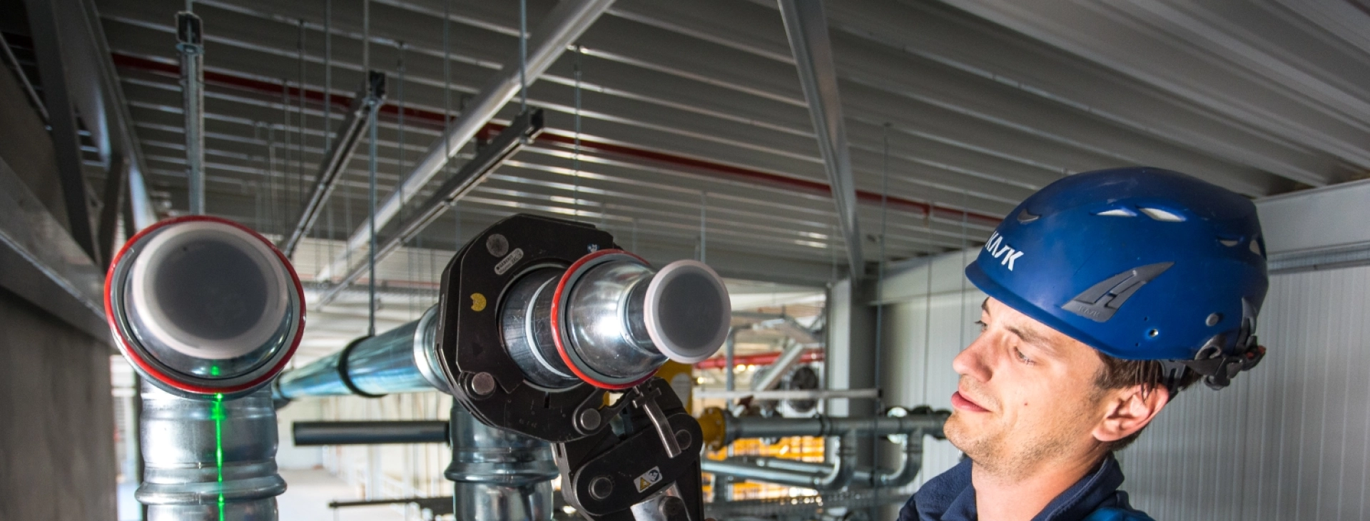 Triaxis-monteur met helm bij leidingwerk in een bedrijfspand